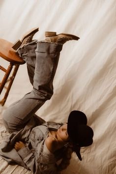 Person in cowboy boots, jeans, and a denim jacket lying on a light fabric