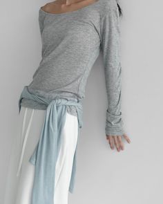 Person in a gray long sleeve shirt and white pants with a light blue fabric tied around the waist