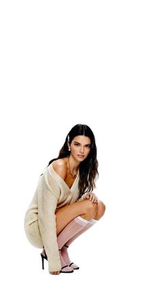 Woman with long dark hair wearing a sweater dress and sheer socks, squatting