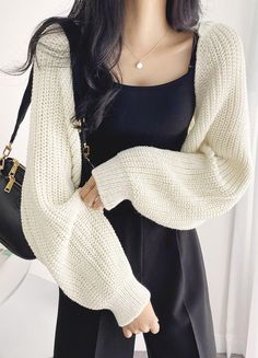 Woman with long black hair wearing a white cardigan and black top
