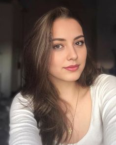 Woman with long brown hair wearing a white top and gold cross necklace