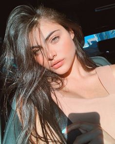 Woman with long dark hair and green eyes in a car, lit by sunlight
