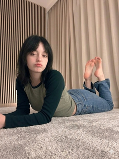 Woman with dark short hair lying on a carpet in jeans and a long sleeve shirt