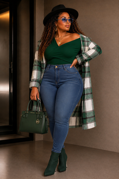 Woman in a plaid coat, jeans, and hat holding a handbag indoors
