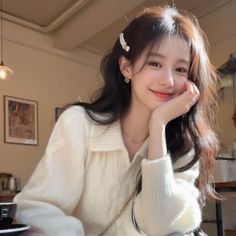 Woman with long hair and a pearl hair clip, wearing a white sweater indoors