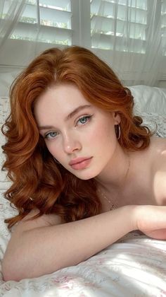 Woman with red hair and blue eyes lying on a bed with soft lighting