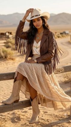 Woman in a cowboy hat and fringe jacket sitting on a fence in the desert at golden hour
