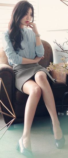 Woman in a light blue shirt and grey skirt sitting on a brown chair