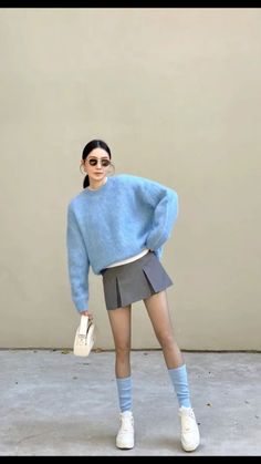 Woman in a blue sweater and pleated skirt posing outdoors