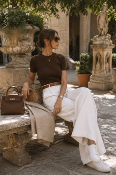Woman in white pants and a brown top sitting on a stone bench outdoors