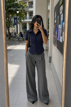 Woman in a striped shirt and wide leg pants taking a mirror selfie on a college campus