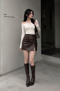 Woman in an off-shoulder top and brown mini skirt with knee-high boots outdoors