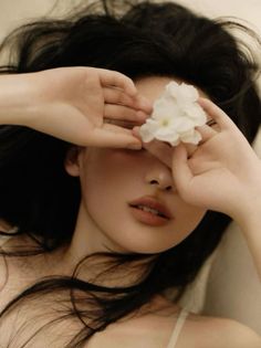 Woman with long black hair covering her eyes with hands and white flowers