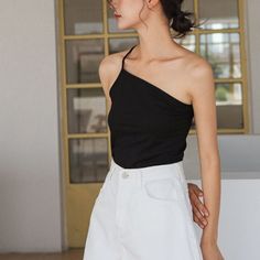 Woman in a black one-shoulder top and white shorts indoors