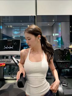 Woman in a white tank top at a gym with a cityscape view at night