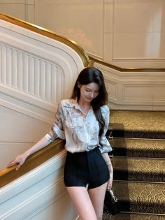 Woman in a patterned shirt and black shorts standing on an elegant staircase