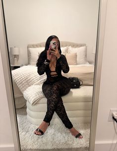 Woman in a black lace jumpsuit taking a mirror selfie in a bedroom