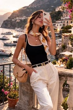 Woman taking a selfie on a balcony overlooking a coastal town at golden hour