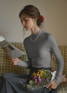 Woman with a red flower in her hair, reading a newspaper and holding flowers