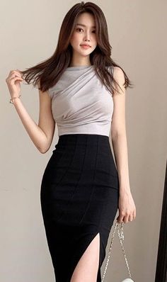 Woman with long hair wearing a grey top and black slit skirt indoors