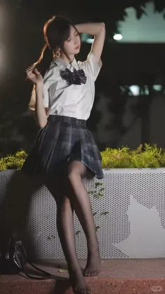 Woman in a school uniform and black pantyhose posing outdoors at night