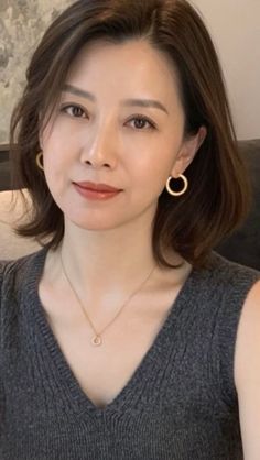 Woman with short brown hair wearing a gray sleeveless top and gold jewelry