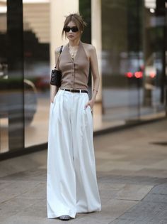 Woman in a brown halter top and white wide-leg pants with sunglasses and a shoulder bag