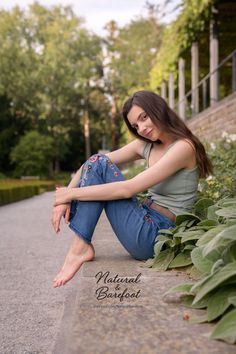 Woman with long hair sitting barefoot on a stone ledge outdoors