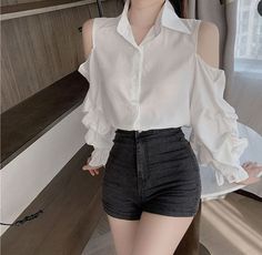 Person wearing a white cold shoulder shirt with ruffle sleeves and high-waisted denim shorts