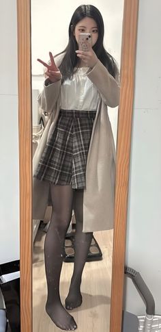 Woman in a plaid skirt and black tights taking a mirror selfie