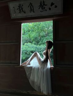 Woman in a sheer dress sitting on a window sill with a forest background