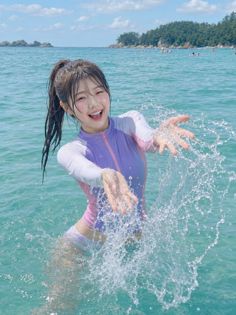 Woman in a purple and pink swimsuit splashing water at the beach