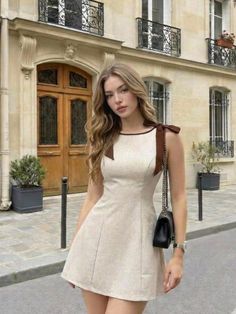 Woman in a beige dress with brown bows standing on a street