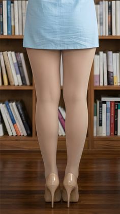 Woman in a light blue dress and nude pantyhose with high heels in front of a bookshelf