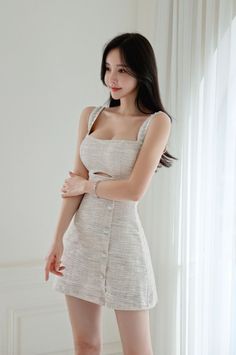 Woman in a light-colored mini dress with a cutout and buttons, standing indoors