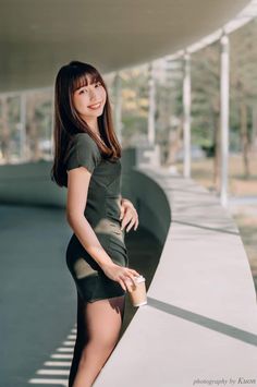 Woman in a short green dress and black tights holding a coffee cup outdoors