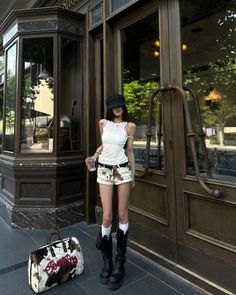 Woman in a white tank top and cow print shorts standing outside a building