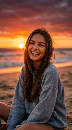 Woman in a grey sweatshirt smiling on a beach at sunset