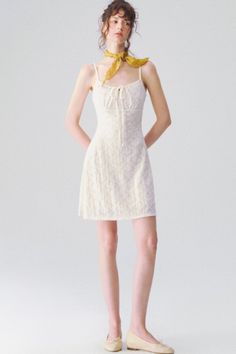 Woman in a white dress and yellow scarf standing against a white background