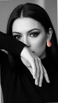 Woman in a black top with an earring, covering her face with her arm