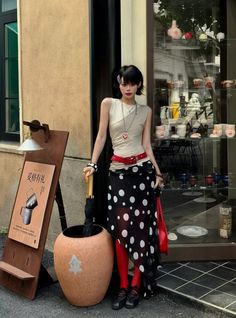 Woman with short black hair wearing a polka dot skirt and red tights outside a storefront