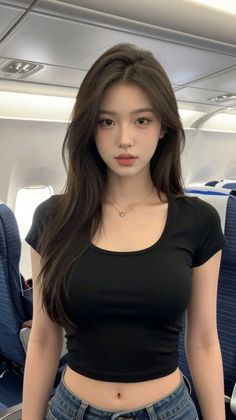 Woman with long dark hair wearing a black crop top and jeans inside an airplane