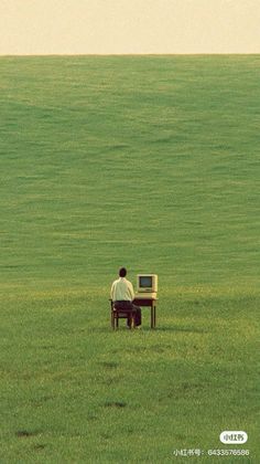 Man sitting at a desk with a computer in a vast green field