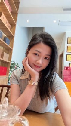 Woman with long dark hair wearing a grey t-shirt and watch, smiling indoors