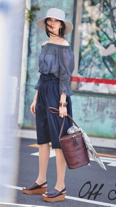 Woman in an off-shoulder top, culottes, and a wide-brim hat holding a handbag