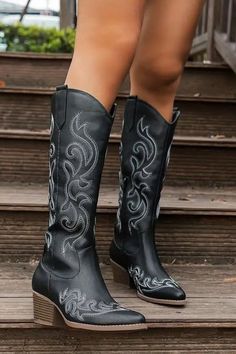 Person wearing black cowboy boots with white embroidery on wooden stairs