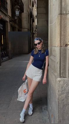 Woman in a bandana and sunglasses leaning against a stone wall on a narrow street