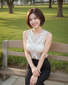 Woman with short hair in a white lace top and black pants sitting on a park bench