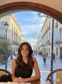 Woman in a black dress smiling at a table with a street view outside