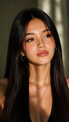 Woman with long dark hair and gold jewelry in soft, warm lighting